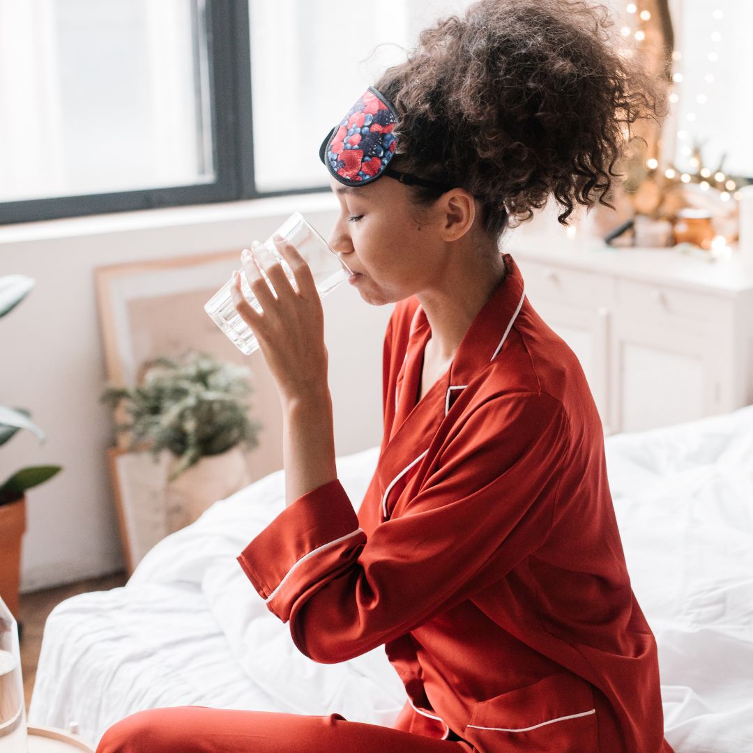 person drinking a glass of water while sitting in bed