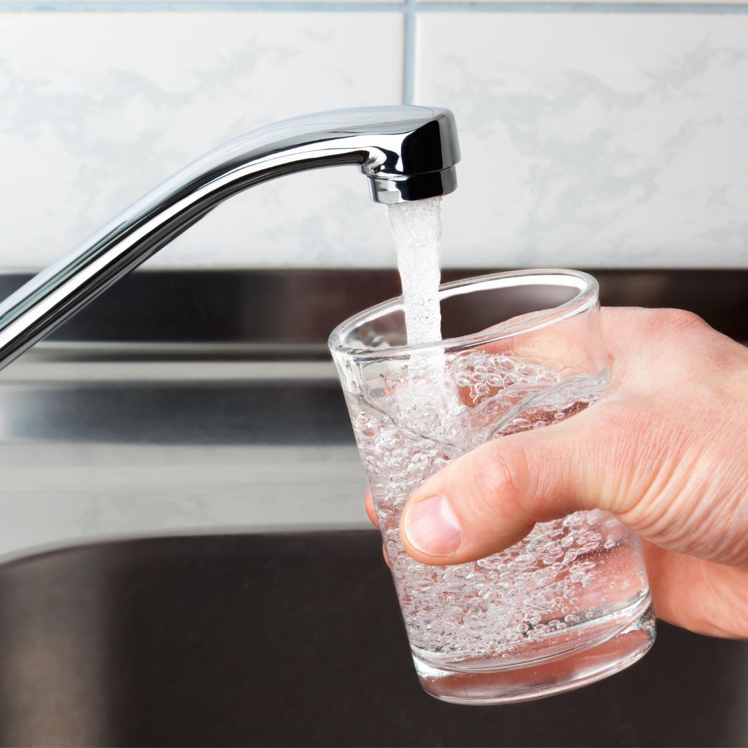 person filling glass with water from faucet