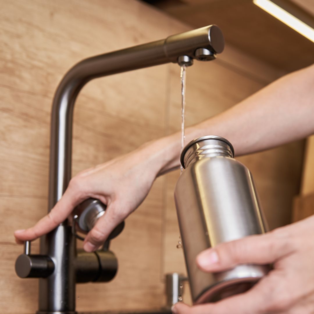 person filling bottle with water from faucet
