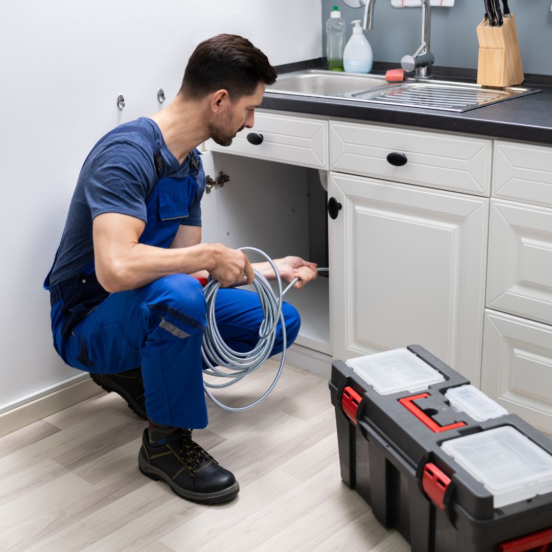 A plumbing using a snaking tool to clean out pipes