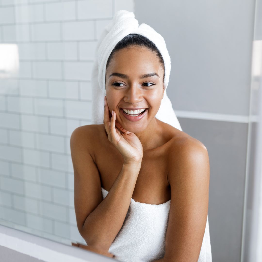 person in a towel smiling at themselves in the bathroom mirror